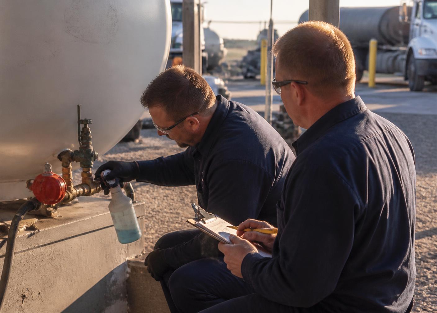 Two propane technicians running a leak check on a bulk tank valve