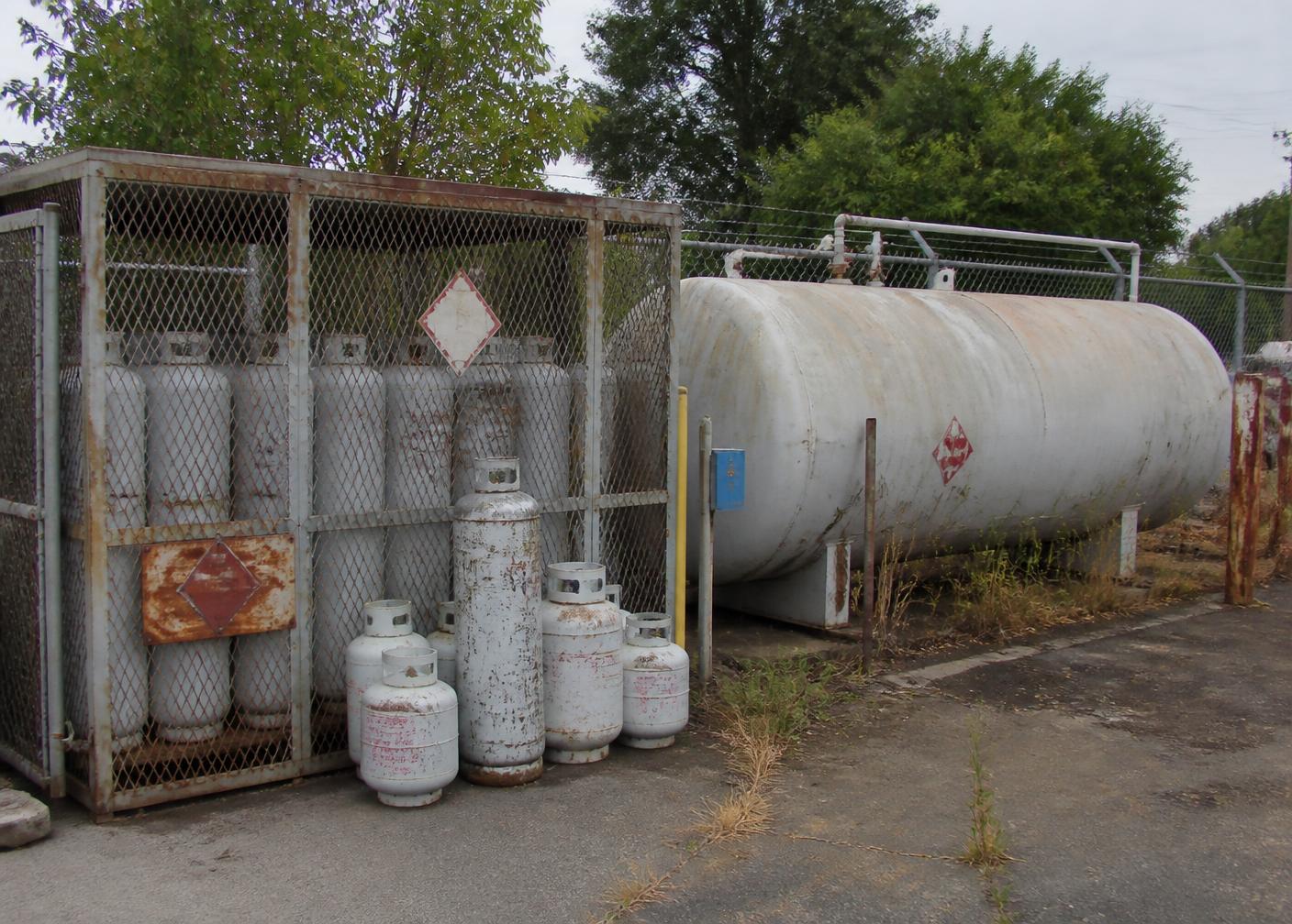 Propane cylinders in a storage cage next to a bulk storage tank